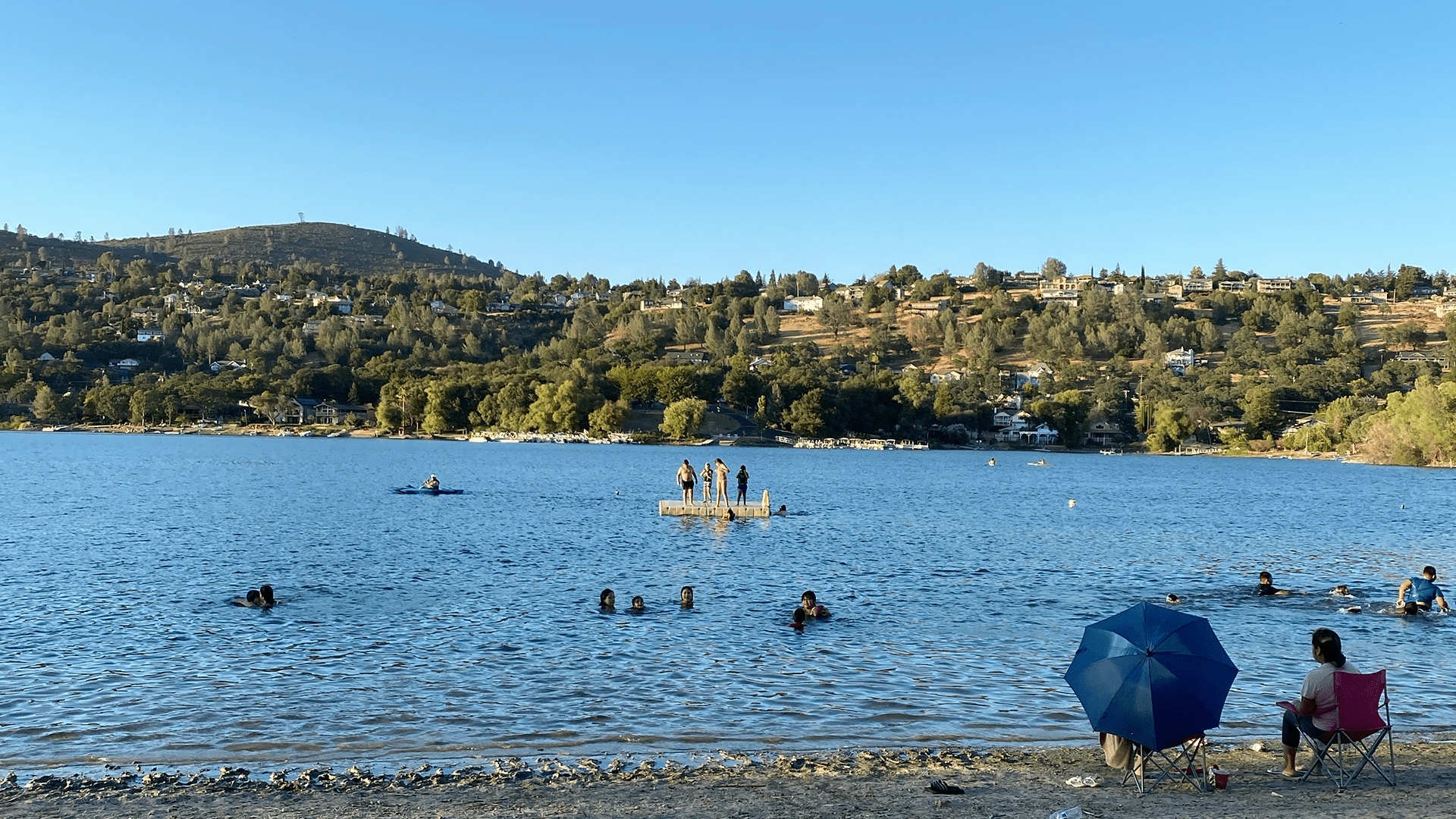 View of Hidden Valley Lake, CA beach with residents swimming and relaxing, showcasing waterfront lifestyle and hillside homes — photo by local real estate agent Jaime Dooley.